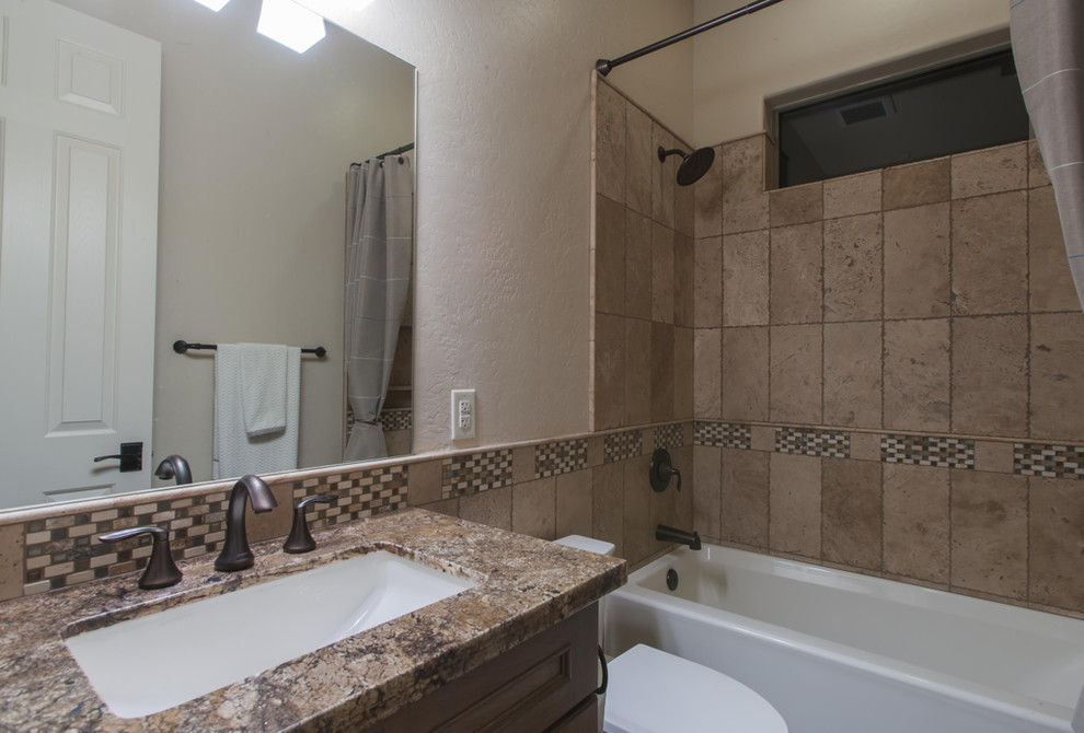 Photo of a small traditional 3/4 bathroom in Phoenix with recessed-panel cabinets, dark wood cabinets, an alcove tub, a shower/bathtub combo, a two-piece toilet, multi-coloured tile, ceramic tile, beige walls, ceramic floors, an undermount sink and granite benchtops.