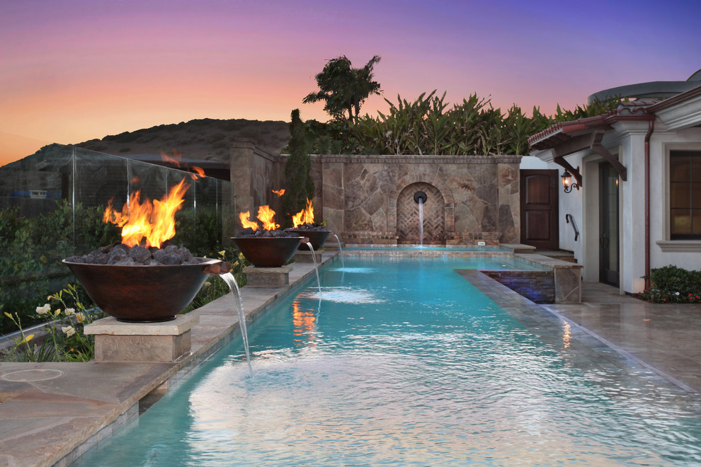 Photo of a large mediterranean backyard custom-shaped lap pool in Orange County with a water feature and natural stone pavers.