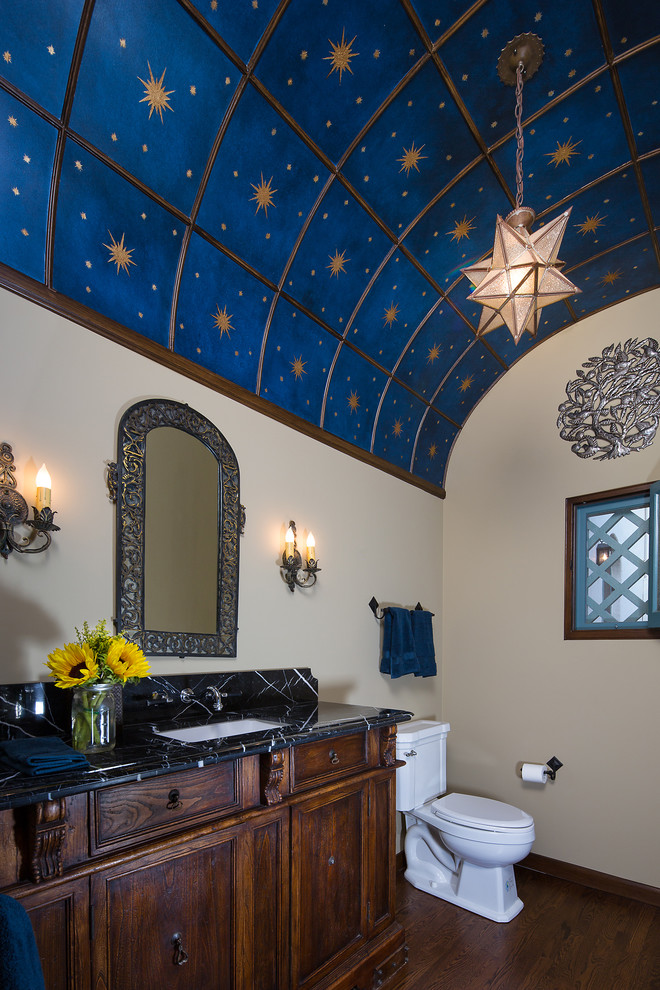 This is an example of a mid-sized mediterranean powder room in Los Angeles with an undermount sink, recessed-panel cabinets, dark wood cabinets, marble benchtops, a two-piece toilet, white walls and medium hardwood floors.