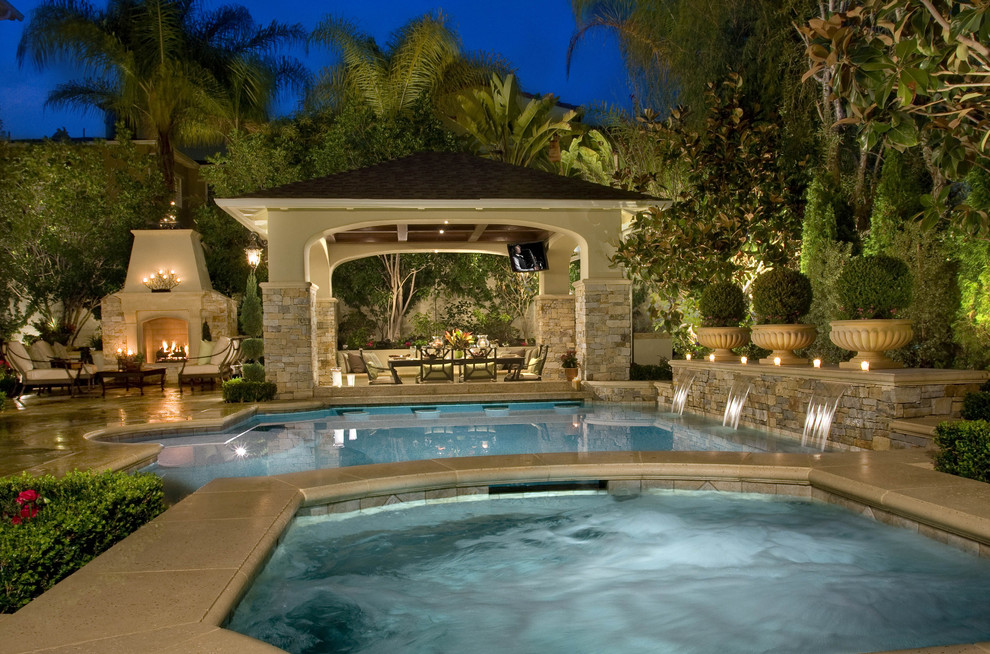 This is an example of a large traditional backyard lap pool in Los Angeles with a water feature and natural stone pavers.