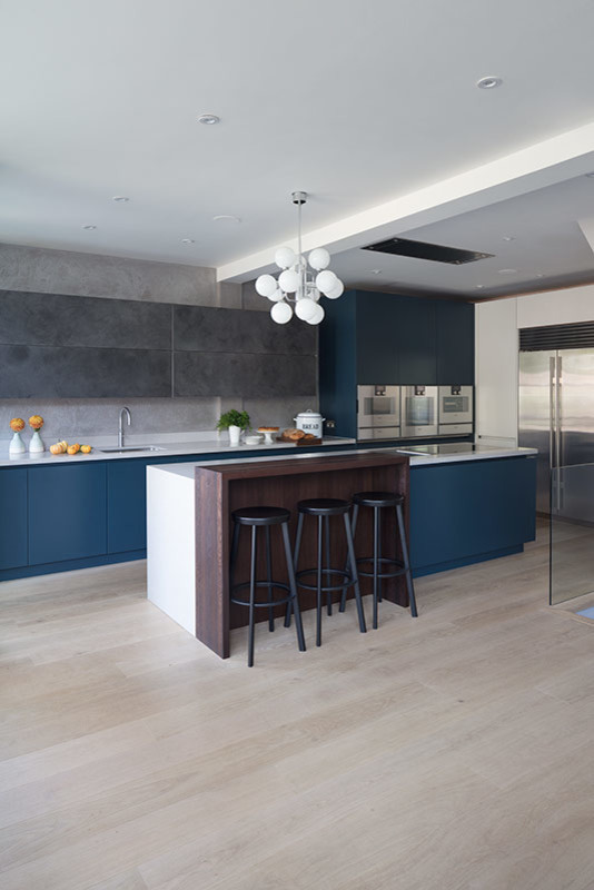 Design ideas for a mid-sized contemporary single-wall eat-in kitchen in London with flat-panel cabinets, blue cabinets, solid surface benchtops, grey splashback, light hardwood floors, with island, beige floor and white benchtop.