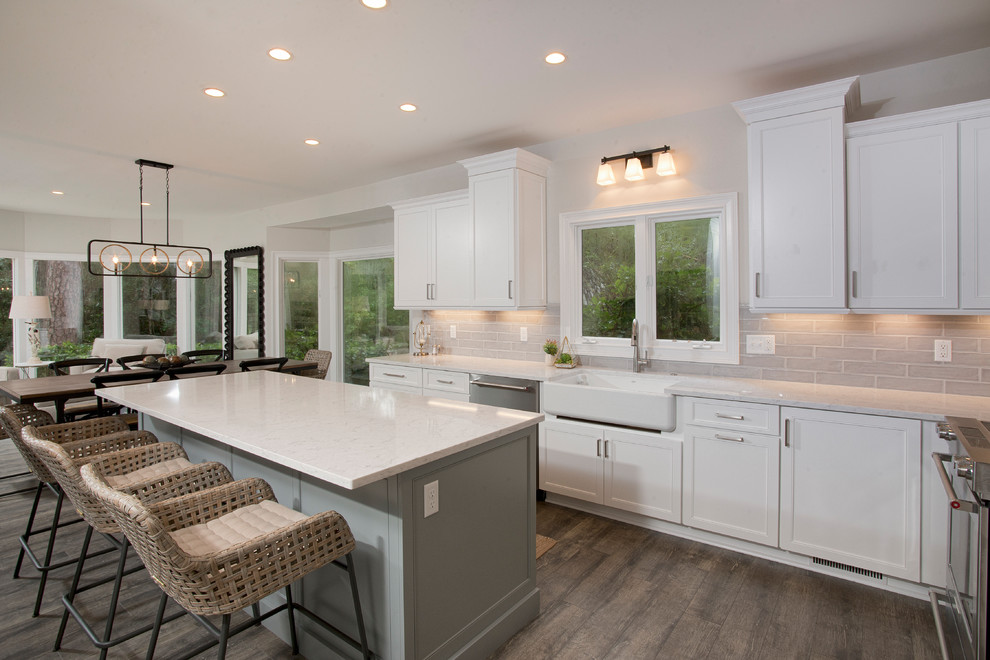 Large transitional u-shaped eat-in kitchen in Charleston with a farmhouse sink, recessed-panel cabinets, white cabinets, quartz benchtops, grey splashback, subway tile splashback, stainless steel appliances, vinyl floors, with island, grey floor and white benchtop.