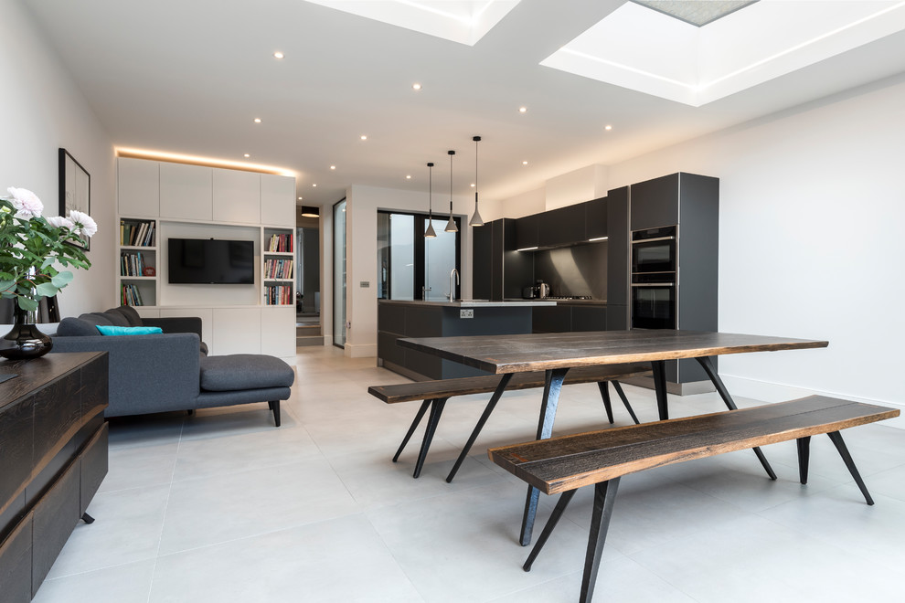 Mid-sized contemporary galley open plan kitchen in London with a drop-in sink, flat-panel cabinets, black cabinets, stainless steel benchtops, metallic splashback, black appliances, porcelain floors, with island and grey floor.