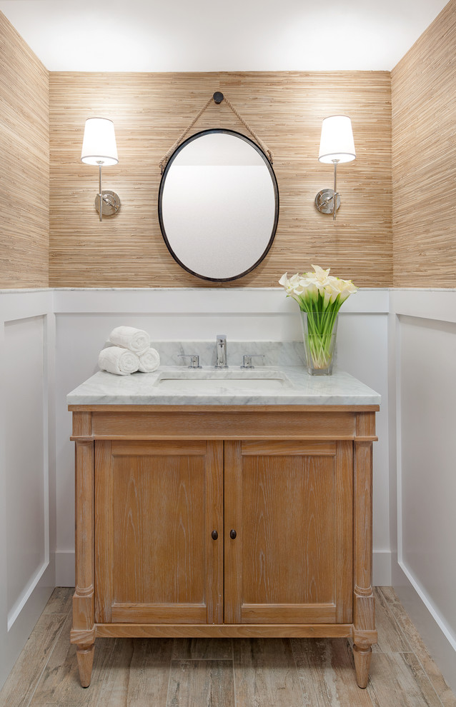 This is an example of a beach style powder room in San Diego with furniture-like cabinets, medium wood cabinets, brown walls, light hardwood floors, an undermount sink and grey benchtops.