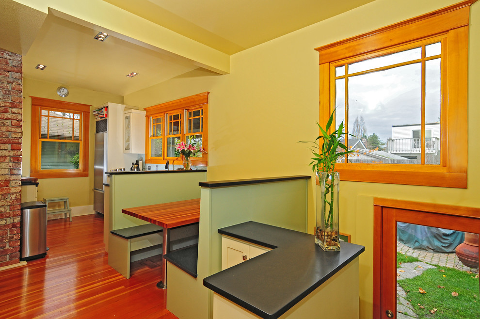 Eat-in kitchen - small transitional u-shaped medium tone wood floor eat-in kitchen idea in Seattle with an undermount sink, glass-front cabinets, white cabinets, white backsplash, ceramic backsplash, stainless steel appliances, yellow walls and no island