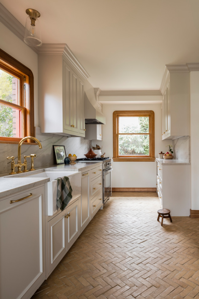 This is an example of a mid-sized transitional galley separate kitchen in Seattle with a farmhouse sink, recessed-panel cabinets, beige cabinets, quartzite benchtops, beige splashback, stone slab splashback, stainless steel appliances, terra-cotta floors, no island, beige floor and beige benchtop.