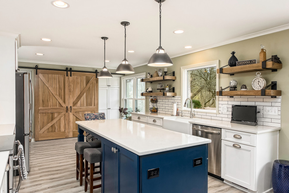 This is an example of a large country kitchen in Columbus with a farmhouse sink, recessed-panel cabinets, white cabinets, quartzite benchtops, white splashback, stainless steel appliances, laminate floors, with island, grey floor and white benchtop.