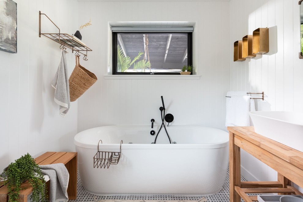 Mid-sized scandinavian master bathroom in Cornwall with light wood cabinets, a freestanding tub, white walls, ceramic floors, wood benchtops, multi-coloured floor, beige benchtops, open cabinets and a vessel sink.