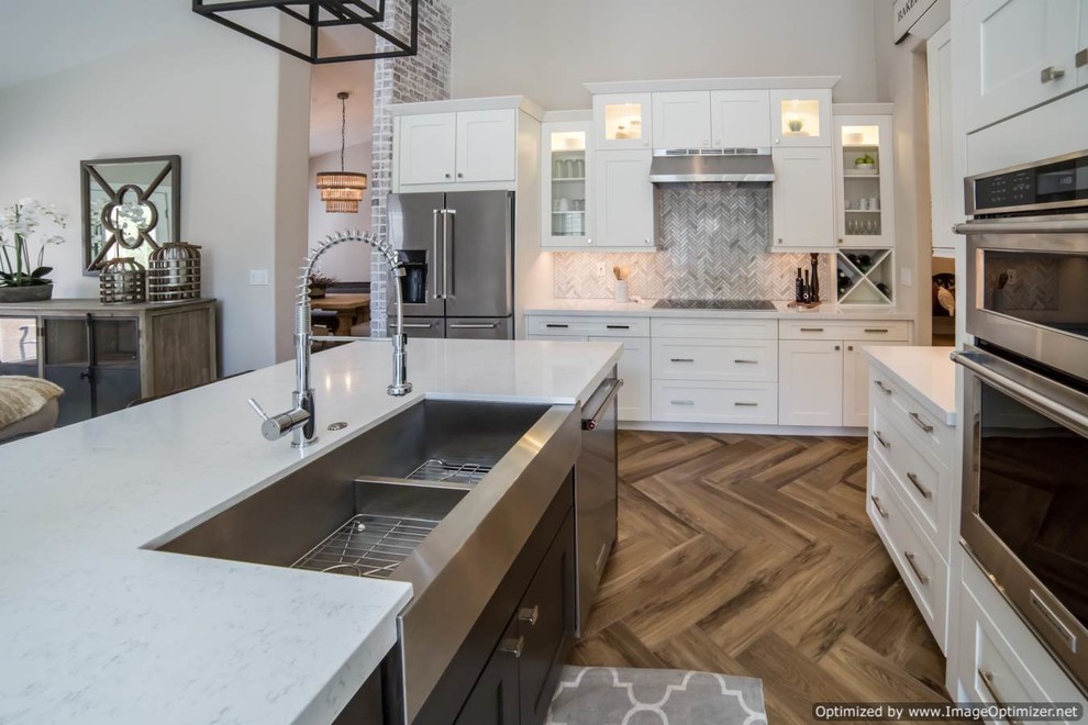 Inspiration for a large traditional l-shaped eat-in kitchen in Phoenix with a farmhouse sink, shaker cabinets, white cabinets, quartzite benchtops, grey splashback, matchstick tile splashback, stainless steel appliances, light hardwood floors and with island.