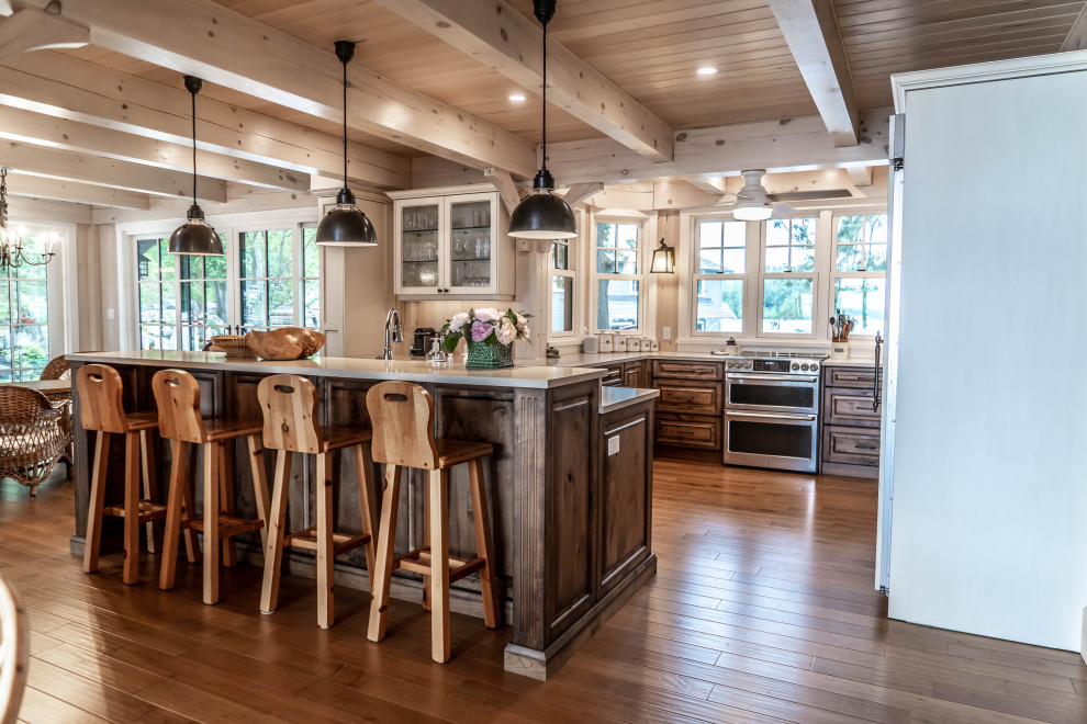 Example of a mid-sized mountain style u-shaped light wood floor and beige floor eat-in kitchen design with an undermount sink, raised-panel cabinets, distressed cabinets, quartz countertops, beige backsplash, wood backsplash, stainless steel appliances, an island and beige countertops