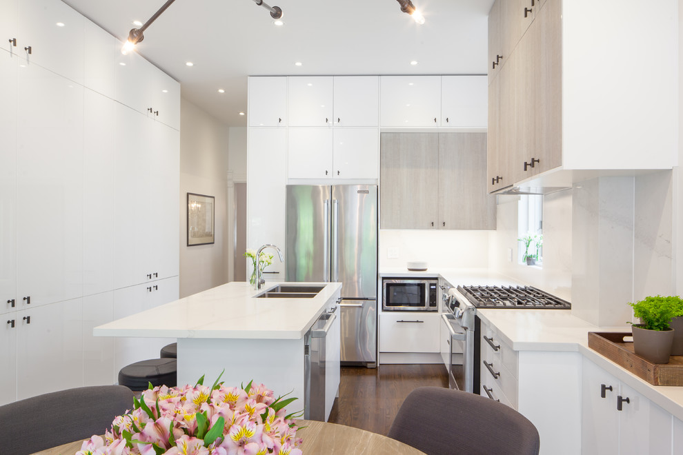 Photo of a mid-sized modern l-shaped eat-in kitchen in Toronto with an undermount sink, flat-panel cabinets, white cabinets, marble benchtops, white splashback, stone slab splashback, stainless steel appliances, medium hardwood floors, with island and brown floor.