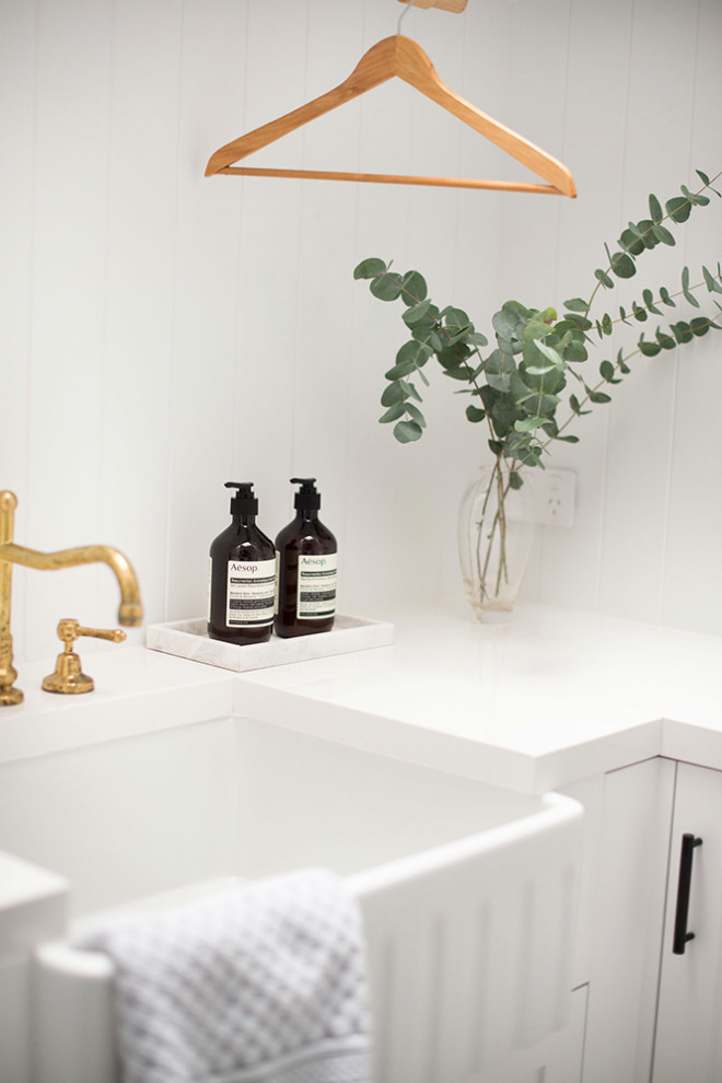 Inspiration for a small utility room in Sydney with a farmhouse sink, shaker cabinets, white cabinets, quartz benchtops, white splashback, white walls, porcelain floors, white benchtop and decorative wall panelling.