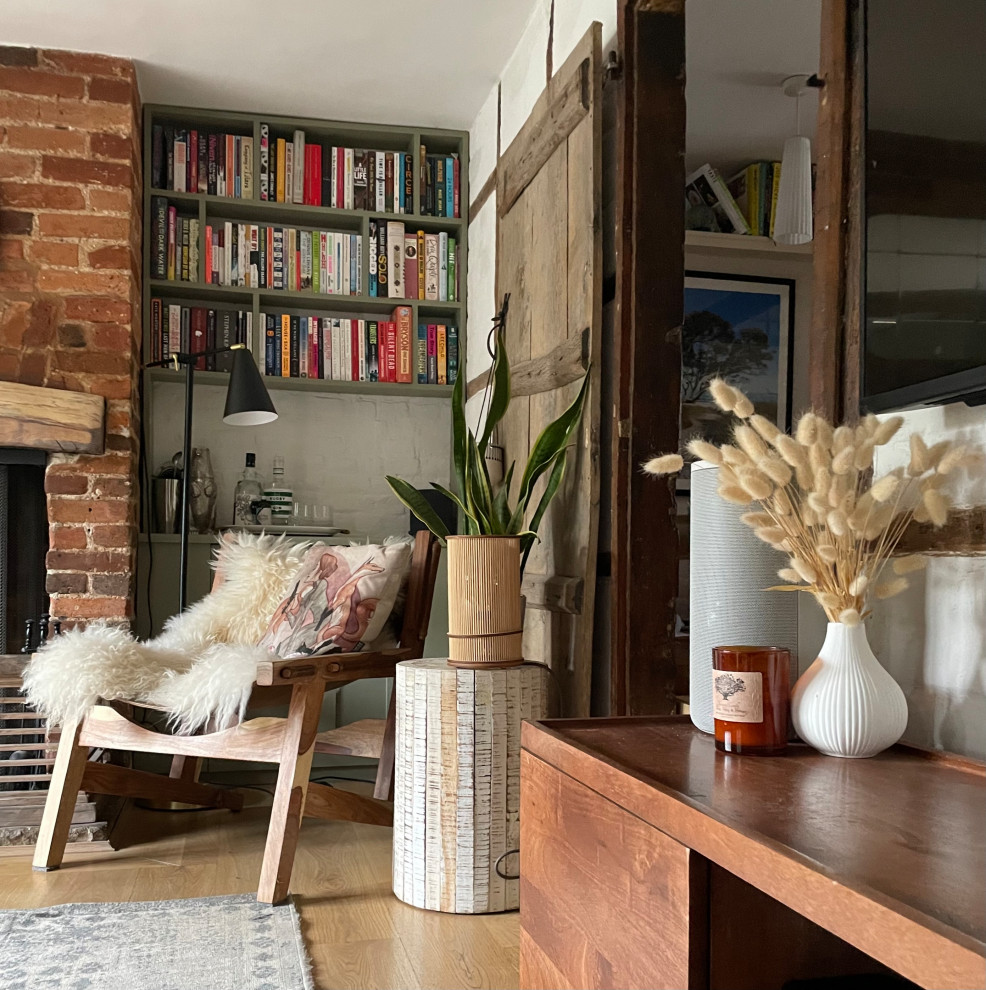 This is an example of a small contemporary enclosed living room in Hertfordshire with a library, white walls, light hardwood floors, a standard fireplace, a brick fireplace surround, a wall-mounted tv, brown floor, exposed beam and brick walls.