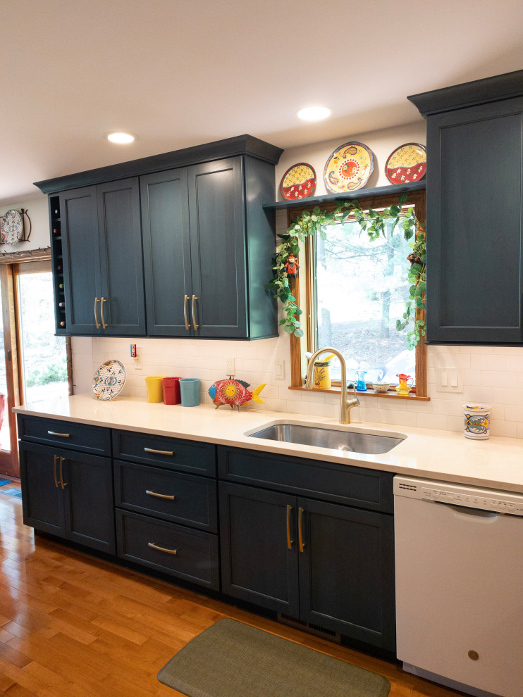 Mid-sized transitional galley light wood floor enclosed kitchen photo with an undermount sink, flat-panel cabinets, blue cabinets, quartz countertops, white backsplash, subway tile backsplash, white appliances, a peninsula and white countertops