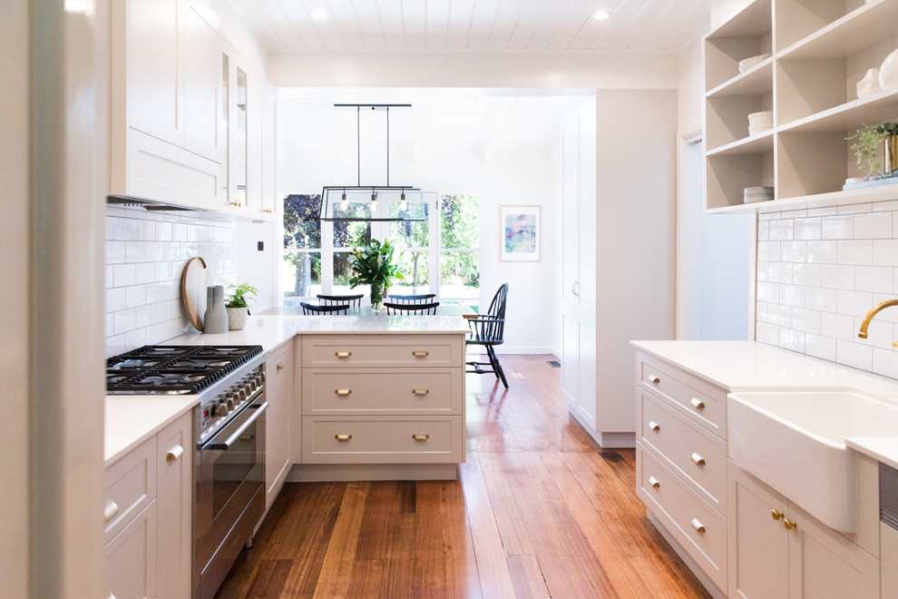 Inspiration for a mid-sized transitional l-shaped kitchen in Melbourne with a farmhouse sink, shaker cabinets, grey cabinets, quartz benchtops, white splashback, subway tile splashback, stainless steel appliances, medium hardwood floors and with island.