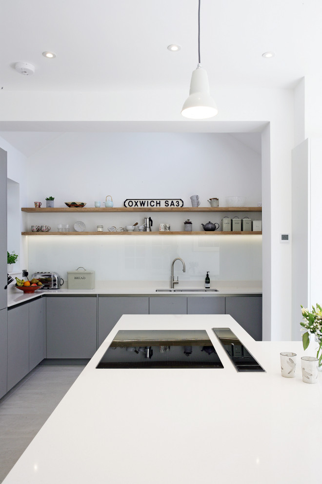Design ideas for a large modern l-shaped eat-in kitchen in Sussex with an integrated sink, flat-panel cabinets, grey cabinets, solid surface benchtops, white splashback, glass sheet splashback, panelled appliances, ceramic floors, with island, grey floor and white benchtop.