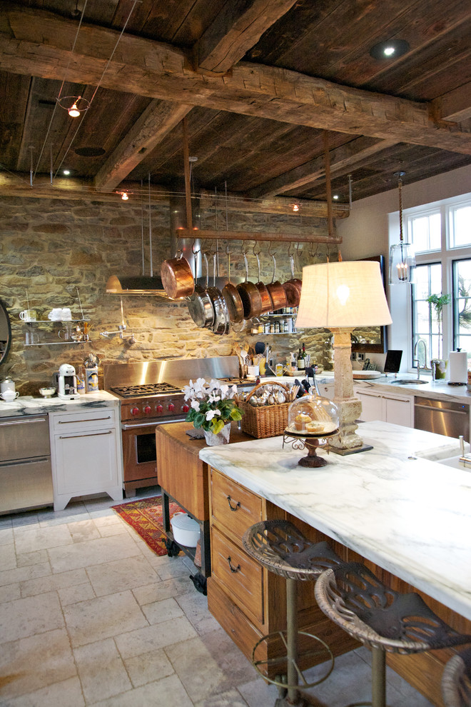 Country kitchen in Philadelphia with a farmhouse sink, distressed cabinets, marble benchtops, stone tile splashback and stainless steel appliances.
