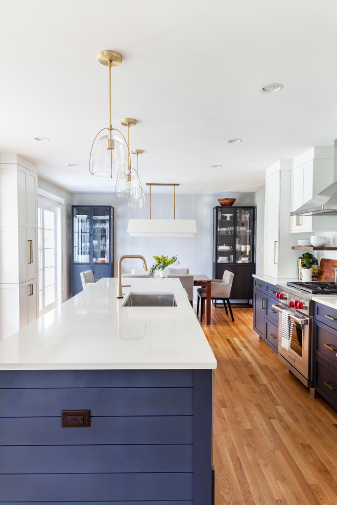 Design ideas for a mid-sized transitional galley eat-in kitchen in Chicago with an undermount sink, shaker cabinets, quartz benchtops, white splashback, stone tile splashback, stainless steel appliances, light hardwood floors, with island, white floor, white benchtop and blue cabinets.