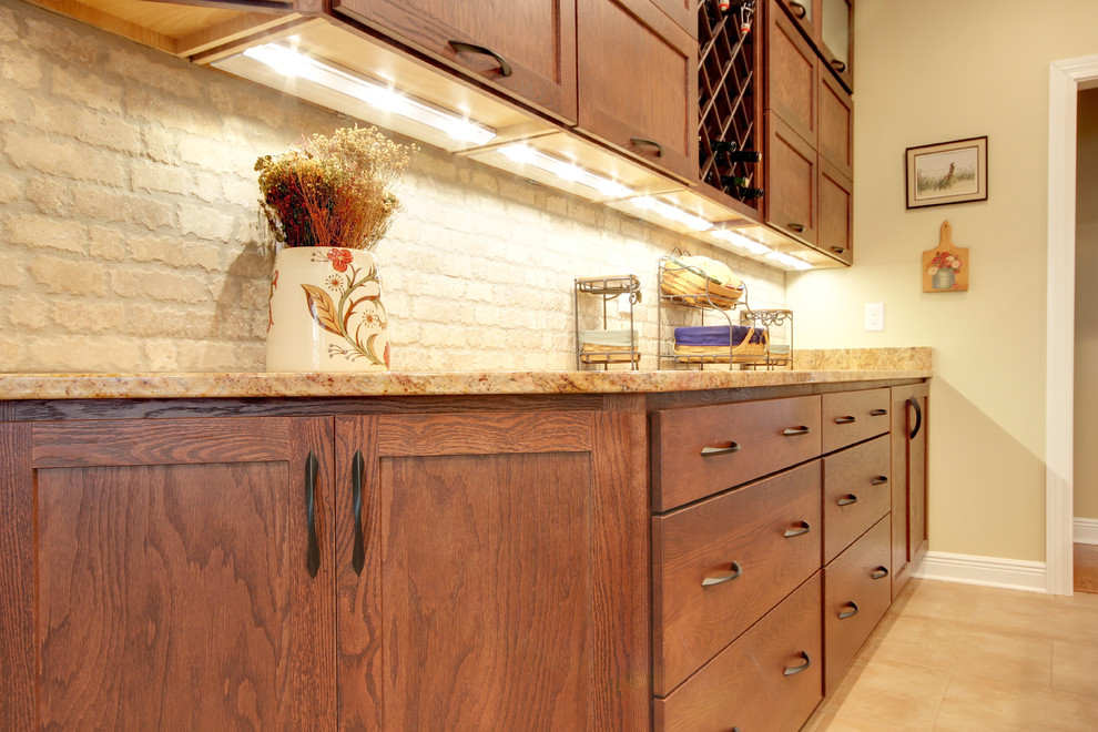 Transitional eat-in kitchen photo in Miami with an undermount sink, shaker cabinets, brown cabinets, granite countertops, beige backsplash, stone tile backsplash and stainless steel appliances