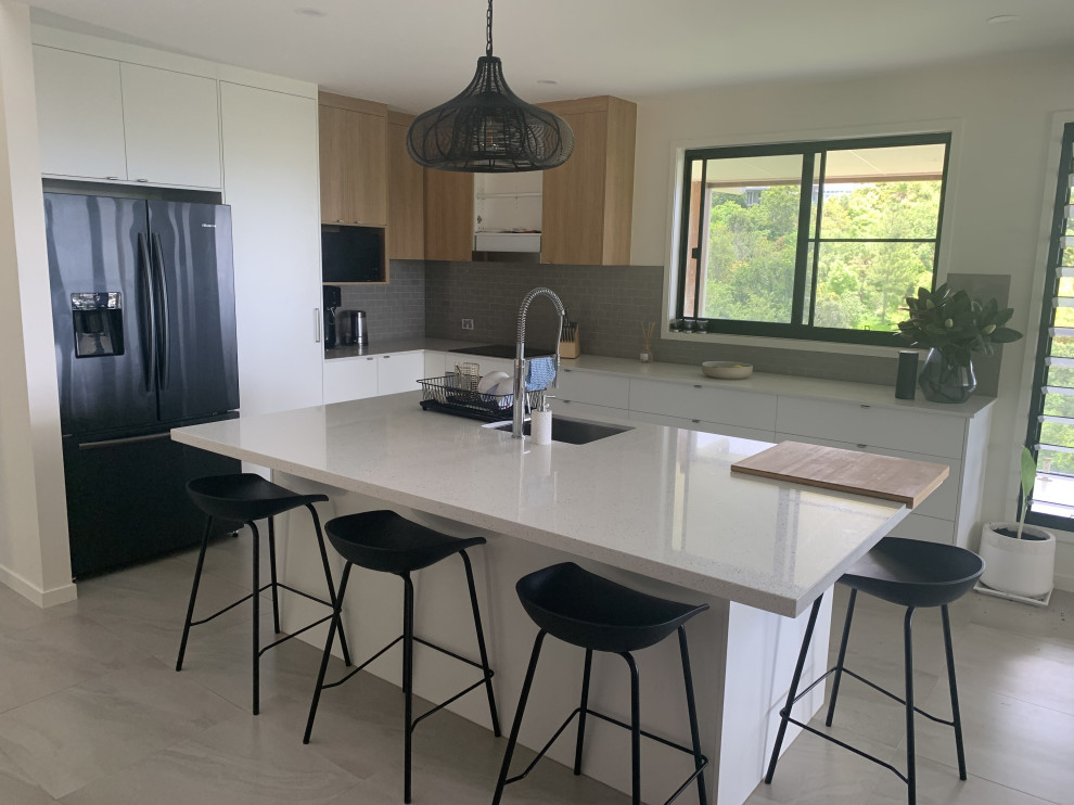 This is an example of a mid-sized modern l-shaped open plan kitchen in Other with an undermount sink, white cabinets, quartz benchtops, beige splashback, subway tile splashback, black appliances, travertine floors, with island, beige floor and white benchtop.