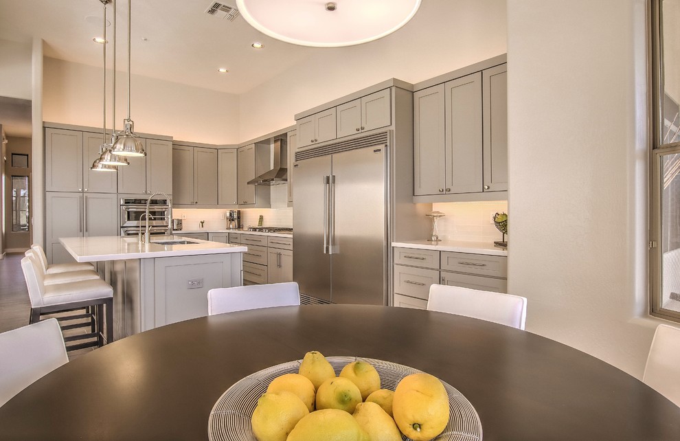 Example of a large transitional l-shaped porcelain tile and brown floor eat-in kitchen design in Phoenix with an undermount sink, shaker cabinets, gray cabinets, quartz countertops, white backsplash, subway tile backsplash, stainless steel appliances, an island and gray countertops