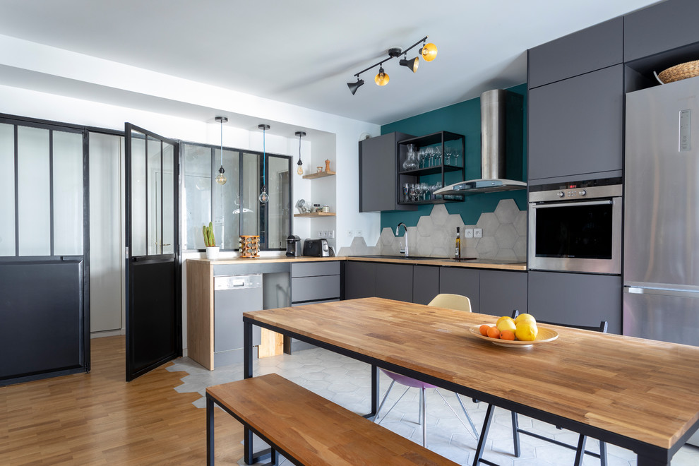 Photo of a contemporary l-shaped eat-in kitchen in Paris with flat-panel cabinets, grey cabinets, wood benchtops, grey splashback, stainless steel appliances, no island and brown benchtop.
