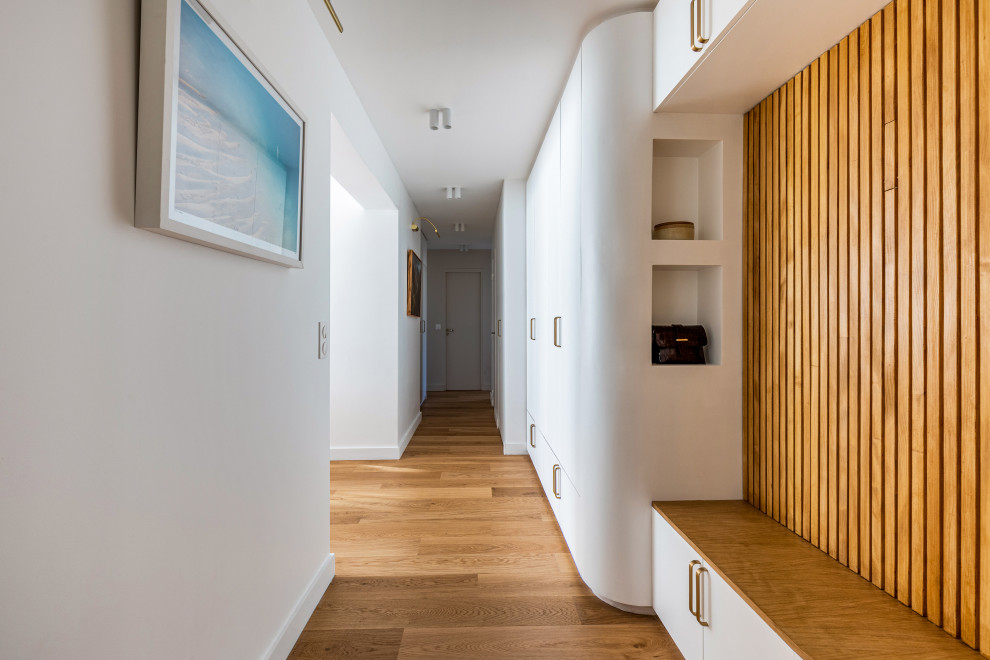Ispirazione per un corridoio minimalista di medie dimensioni con pareti bianche, parquet chiaro, una porta bianca e pavimento marrone