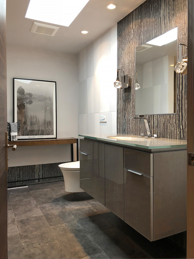 Inspiration for a mid-sized modern 3/4 bathroom in Seattle with glass-front cabinets, grey cabinets, a curbless shower, a wall-mount toilet, black and white tile, stone tile, white walls, porcelain floors, an integrated sink, glass benchtops, grey floor, a hinged shower door and grey benchtops.