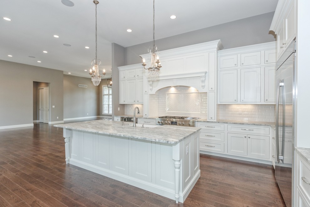 Inspiration for a large transitional l-shaped open plan kitchen in St Louis with a farmhouse sink, shaker cabinets, white cabinets, marble benchtops, white splashback, subway tile splashback, stainless steel appliances, medium hardwood floors, with island and brown floor.
