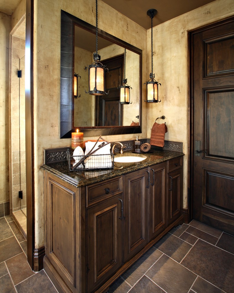 Design ideas for a mid-sized mediterranean 3/4 bathroom in Phoenix with an undermount sink, recessed-panel cabinets, dark wood cabinets, granite benchtops, an alcove shower, beige walls, slate floors, metal tile, gray tile, grey floor, a one-piece toilet and a hinged shower door.