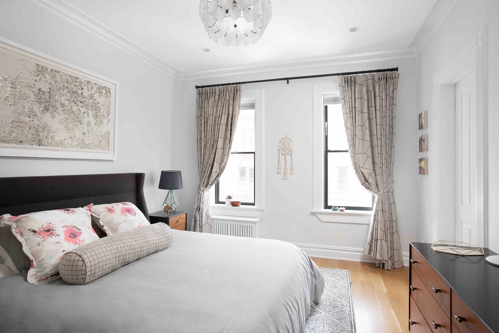 This is an example of a large transitional master bedroom in New York with grey walls, light hardwood floors and brown floor.