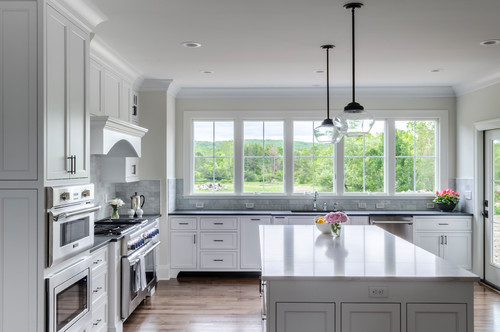 L shaped open concept kitchen with white shaker kitchen cabinets, large island and wide windows overlooking green landscape