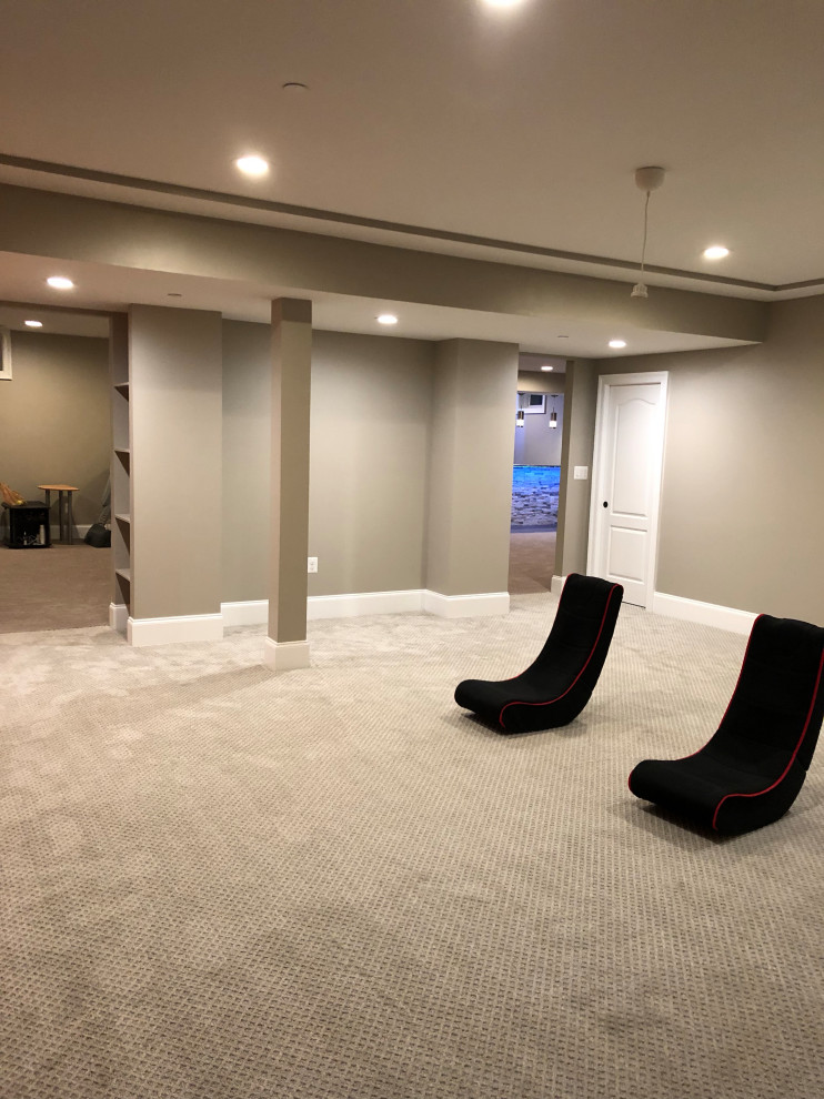 Photo of a large modern look-out basement with grey walls, carpet, a ribbon fireplace, a stone fireplace surround and beige floor.