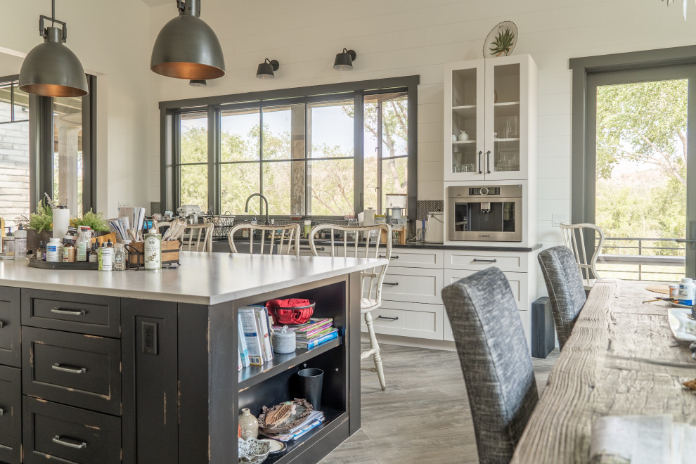 Country eat-in kitchen with a farmhouse sink, shaker cabinets, white cabinets, black splashback, mosaic tile splashback, with island, grey floor and black benchtop.
