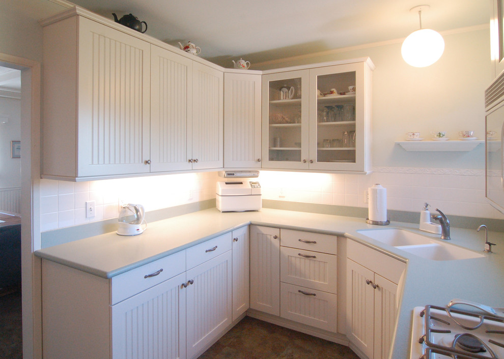 サンルイスオビスポにある小さなシャビーシック調のおしゃれなキッチン (一体型シンク、インセット扉のキャビネット、白いキャビネット、人工大理石カウンター、白いキッチンパネル、ガラスタイルのキッチンパネル、白い調理設備、リノリウムの床) の写真