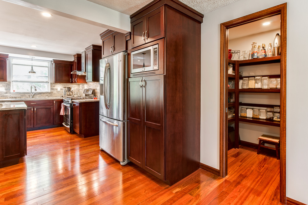 Example of a large transitional l-shaped medium tone wood floor eat-in kitchen design in Los Angeles with an undermount sink, recessed-panel cabinets, dark wood cabinets, granite countertops, gray backsplash, stone tile backsplash, stainless steel appliances and an island