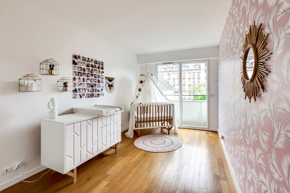 Photo of a small contemporary nursery for girls in Paris with pink walls, medium hardwood floors and brown floor.
