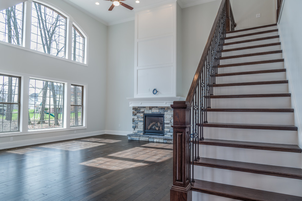 Example of a large transitional open concept dark wood floor and brown floor home design design with gray walls, a standard fireplace, a stone fireplace and a wall-mounted tv