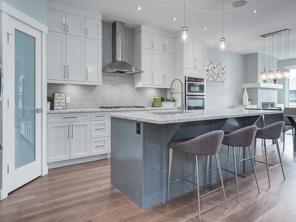 Mid-sized transitional l-shaped light wood floor eat-in kitchen photo in Calgary with a double-bowl sink, beaded inset cabinets, gray cabinets, quartzite countertops, gray backsplash, ceramic backsplash, stainless steel appliances and an island