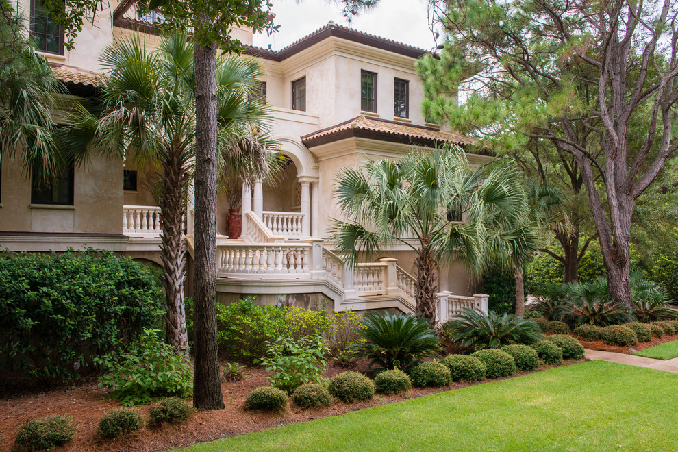 Large mediterranean three-storey stucco beige house exterior in Charleston with a hip roof and a shingle roof.