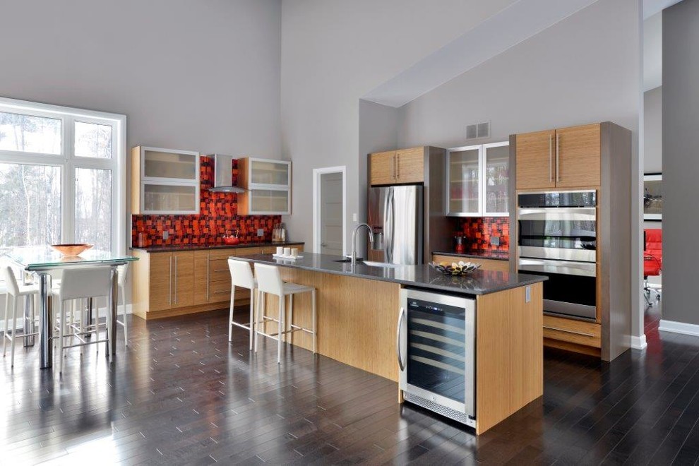 Photo of a large contemporary l-shaped eat-in kitchen in Toronto with a farmhouse sink, flat-panel cabinets, light wood cabinets, limestone benchtops, red splashback, mosaic tile splashback, stainless steel appliances, dark hardwood floors, with island, brown floor and grey benchtop.