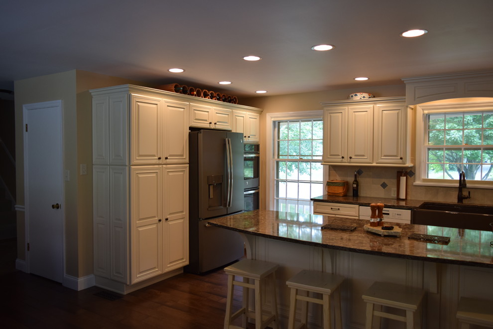 Inspiration for a transitional medium tone wood floor and brown floor kitchen remodel with a farmhouse sink, raised-panel cabinets, white cabinets, quartz countertops, beige backsplash, ceramic backsplash, black appliances and an island