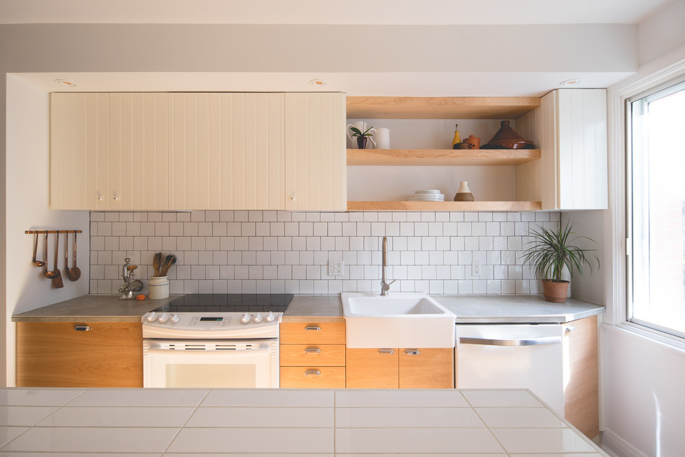 Design ideas for a mid-sized contemporary single-wall kitchen in Montreal with flat-panel cabinets, medium wood cabinets, tile benchtops, white splashback, ceramic splashback, white appliances, with island and a farmhouse sink.
