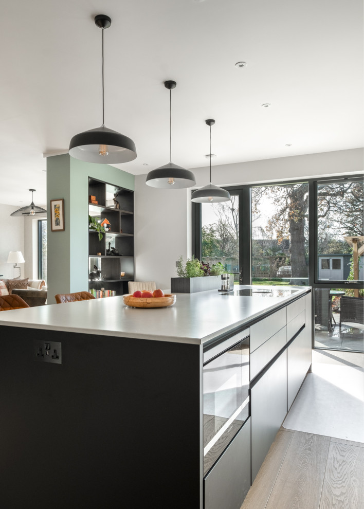 Inspiration for a large contemporary eat-in kitchen in Gloucestershire with a drop-in sink, flat-panel cabinets, black cabinets, solid surface benchtops, white splashback, black appliances, with island and white benchtop.
