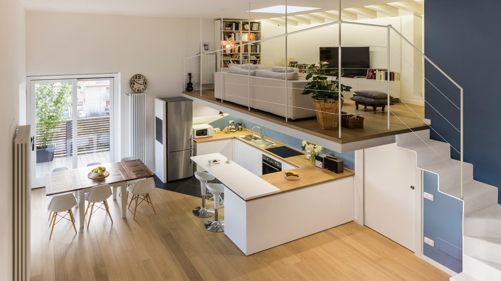 This is an example of a large scandinavian u-shaped eat-in kitchen in Milan with a drop-in sink, flat-panel cabinets, white cabinets, wood benchtops, blue splashback, stainless steel appliances, porcelain floors, multiple islands and grey floor.