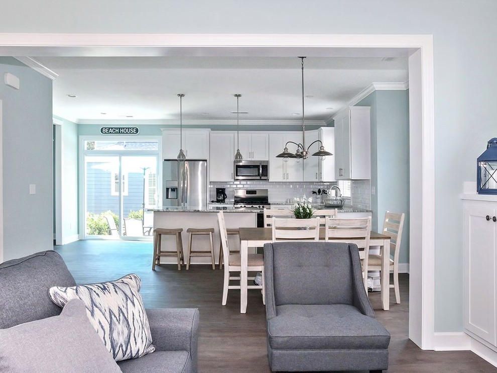 This is an example of a mid-sized beach style l-shaped eat-in kitchen in Other with a single-bowl sink, shaker cabinets, white cabinets, quartz benchtops, white splashback, subway tile splashback, stainless steel appliances, medium hardwood floors, with island, brown floor and grey benchtop.