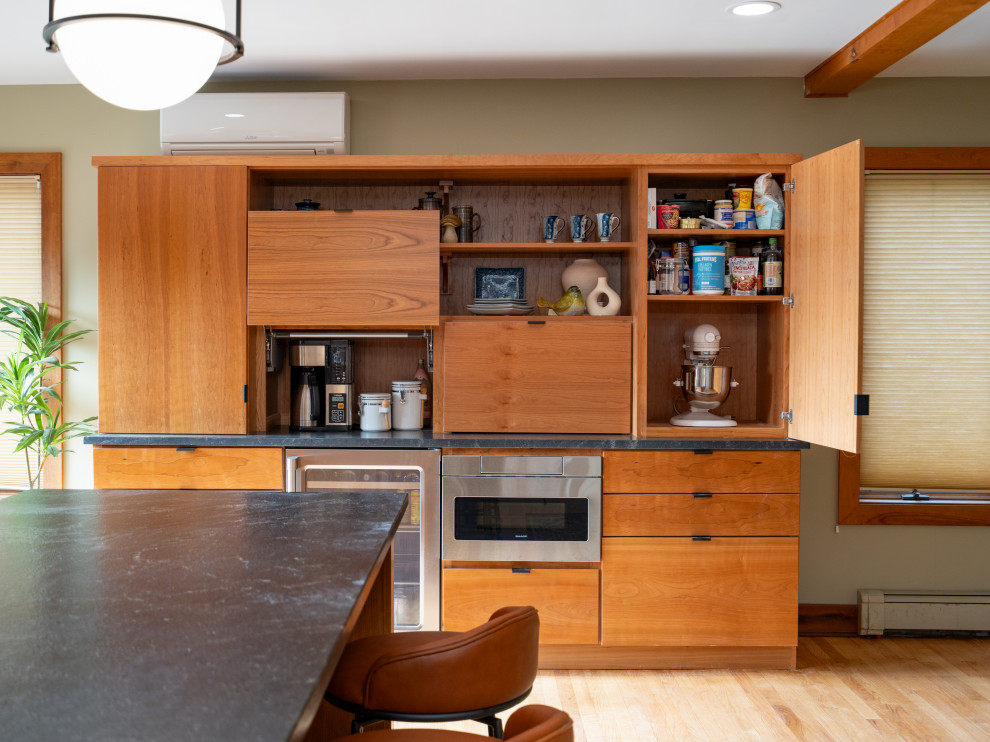 Example of a large trendy galley light wood floor kitchen design with a single-bowl sink, flat-panel cabinets, granite countertops, black backsplash, granite backsplash, stainless steel appliances, an island and black countertops