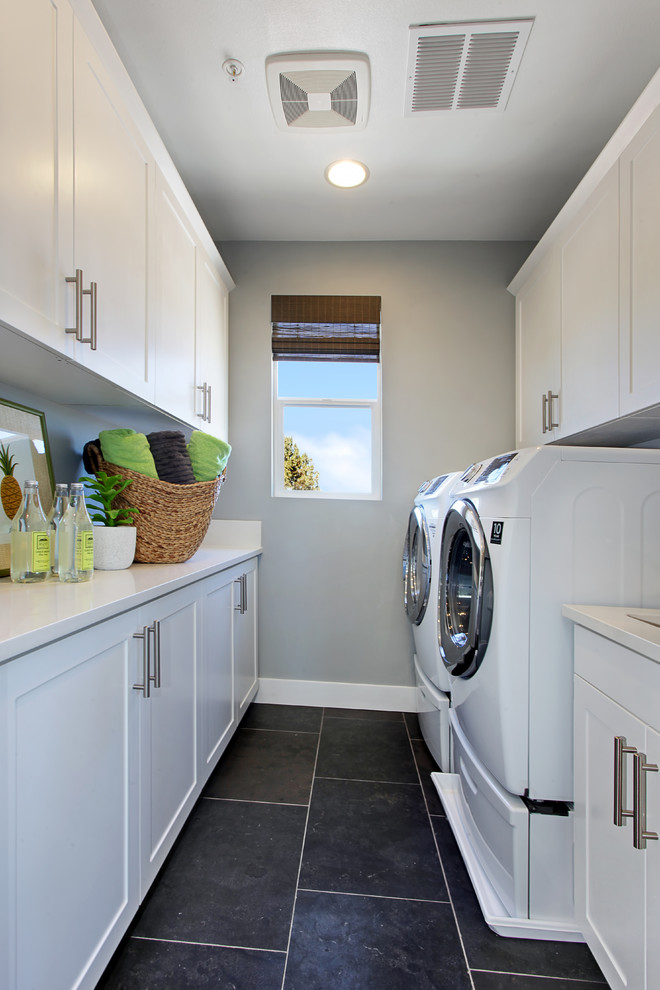 Transitional galley laundry room in Orange County with shaker cabinets, white cabinets, grey walls, a side-by-side washer and dryer, black floor and white benchtop.