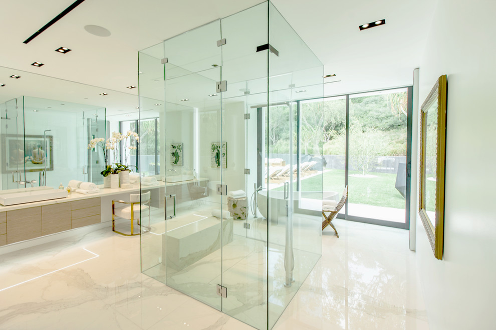 This is an example of a contemporary master bathroom in Los Angeles with flat-panel cabinets, light wood cabinets, a freestanding tub, white walls, marble floors, marble benchtops, a curbless shower, a vessel sink and a hinged shower door.