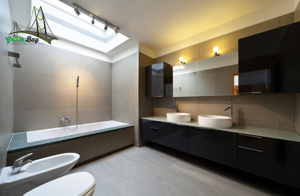 Inspiration for a mid-sized contemporary master bathroom in San Francisco with flat-panel cabinets, a drop-in tub, gray tile, black cabinets, a bidet, beige walls, painted wood floors, a vessel sink and glass benchtops.